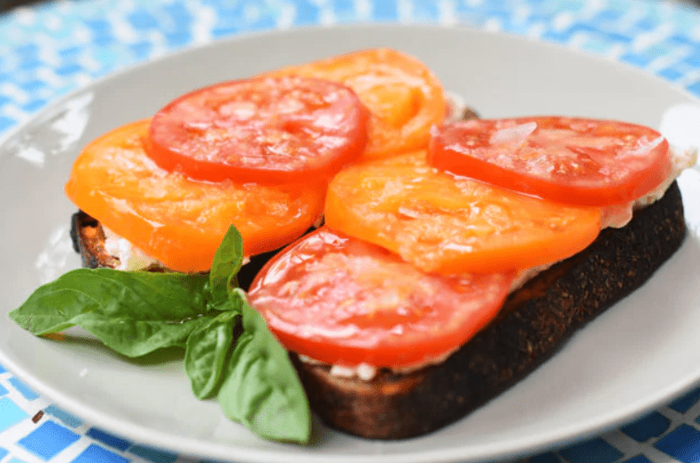 Tomatoes on toast with a sprig of basil on a white plate.