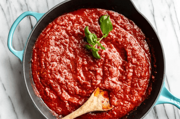 A pan filled with red marinara sauce, garnished with a bright green basil leaf