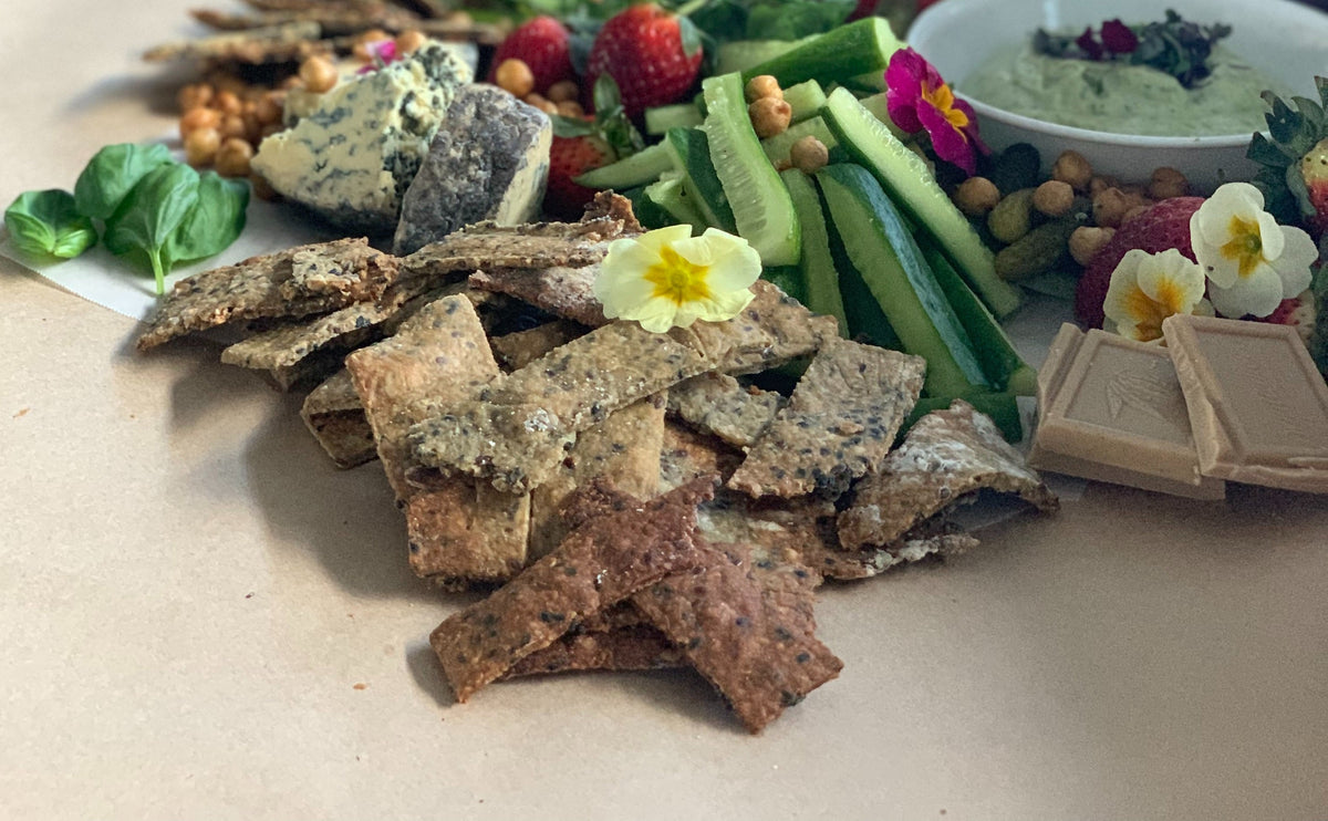 Flaxseed crackers piled on a table among various flowers, cheeses, chocolates, and dips.