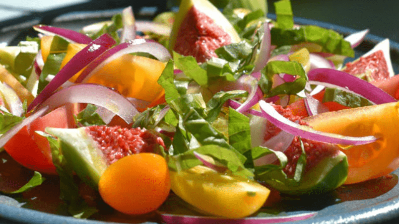 Figs, tomatoes, red onion, and basil on a blue plate