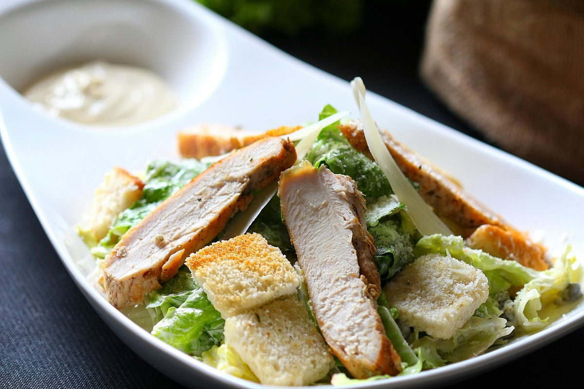 Roast chicken and bread sitting among greens in a bowl
